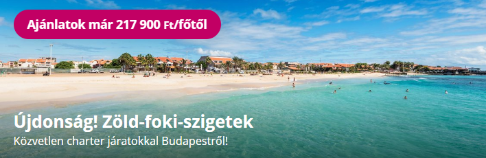 Tengerparti panoráma zöld türkiz vízzel, homokos parttal és távoli városrésszel kék égen.